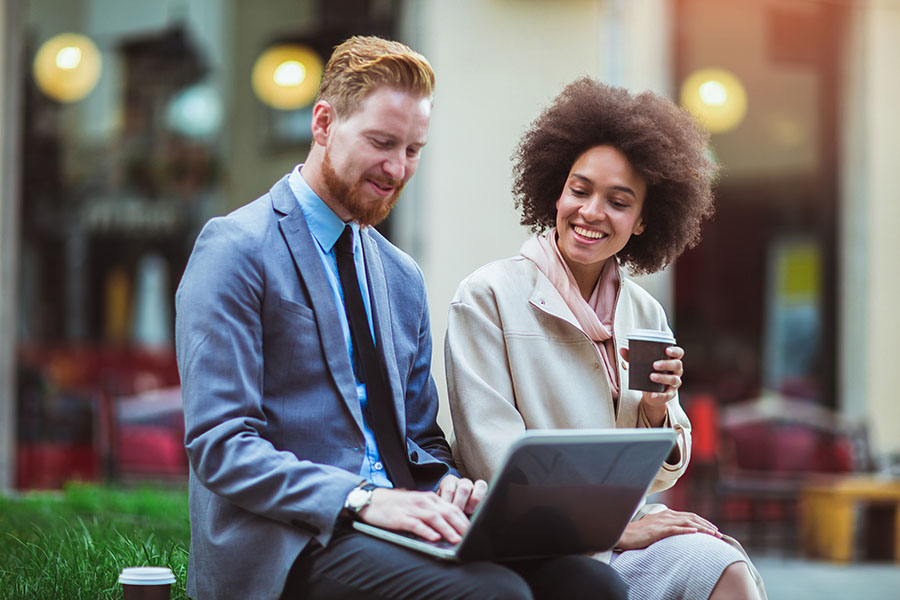 Blog - Young Coworkers Reading Laptop on A Bench With Coffee